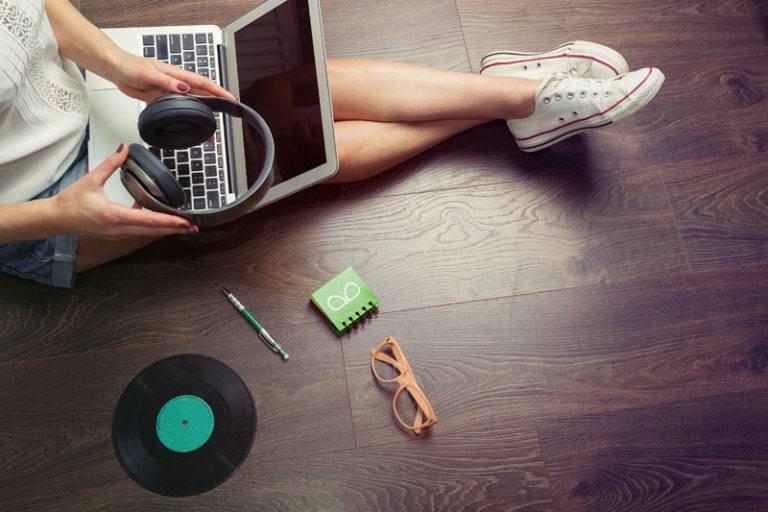 Woman listening to music on laptop sat on dark vinyl floor